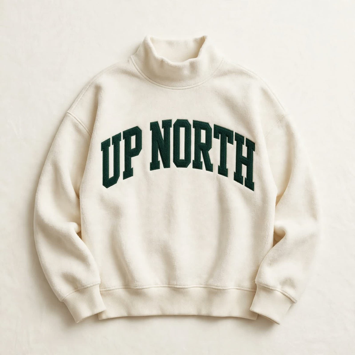 UP NORTH mock neck sweatshirt laid flat, cream with forest green varsity letters